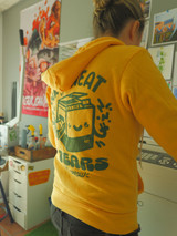 Image of a person from behind at a risograph printer  wearing the product hoodie [zip option] hoodie is golden yellow with a hood and dark green ink printed on back. image printed on back is a printer with the words "ink, sweat, and tears": & "split arrow" underneath