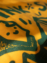 zoomed in image of a portion of the printed hoodie design in green ink on a gold yellow hoodie. Design portion is of paper with a smily face