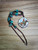 Retro illustrated multicolor roping cowboy design on 2.25 inch natural bone base
Sterling silver setting with rope detail border
20 inch strand with turquoise flakes, flat cateye beads, and small round wood beads