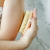 A woman holding a Natural Sisal Body Brush against her arm