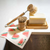 A Swedish dish cloth, wooden dish brush, dish soap block, and pot scrubber on display