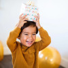 A child holding a gift wrapped in compostable and reversible happy birthday wrapping paper on his head