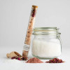 Natural rose sandalwood bath soak in a glass vial with cork closure leaning against glass jar