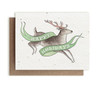 A card embedded with seeds with a watercolor design of a jumping reindeer with the saying "Happy Holidays" and a kraft paper envelope on a blank white background