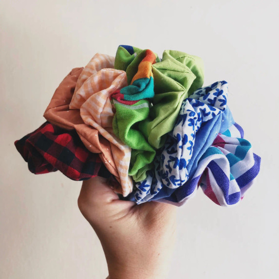 A hand holding up multiple upcycled scrunchies in varying colors against a white background