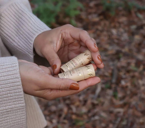 A woman holding two different plastic-free vegan tinted lip balm with fall leaves on the ground