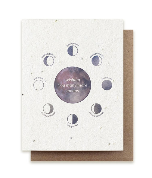 A plantable birthday card embedded with herb seeds and a purple watercolor design of moon phases saying "wishing you many more moons" with a kraft envelope