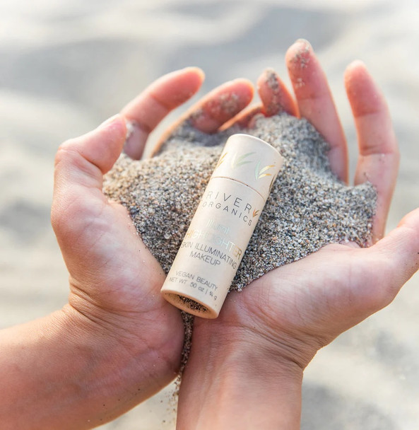 Hands cupping sand on beach with a highlighter in a paper tube