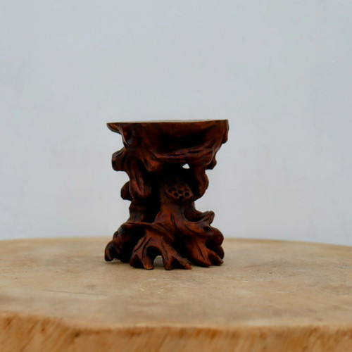 A meticulously hand-carved wooden bonsai and succulent display stand, identified as No. 68, rests on a light-colored wooden surface against a plain, off-white background. The stand is crafted from a dark, polished wood with a rich reddish-brown hue and a smooth, satin finish. Its design intricately mimics the natural, gnarled appearance of a weathered tree root, featuring an irregular, spreading base with several root-like feet. The central body of the stand is highly textured with organic shapes, including small holes and a cluster of tiny, carved seed pods reminiscent of a lotus. A small, flat, circular platform at the top provides a level surface for displaying miniature bonsai trees, succulents, or other small decorative items. The craftsmanship emphasizes the beauty of natural wood grain and rustic aesthetics, making it a functional and artistic piece of decor for plant enthusiasts.