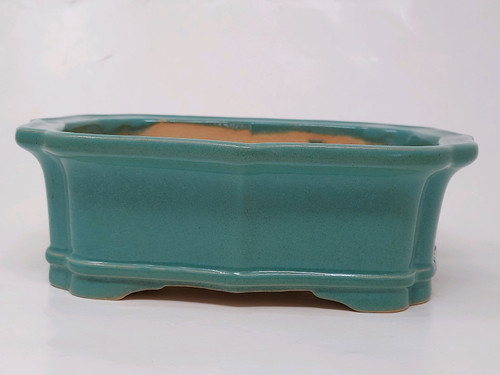 A side profile of a 7-inch glazed Yixing bonsai pot, showcasing its rich teal or turquoise glossy finish. This rectangular pot features a distinctive lobed design with inward-curving corners and a subtle double-stepped lip at both the top rim and the base. The vessel is elevated on four integrated, low-profile feet that provide a small gap for drainage and airflow. The interior of the pot remains unglazed, exposing the pale tan color of the natural Yixing clay. Set against a clean, neutral white background, the pot's elegant proportions and vibrant glaze make it an ideal ceramic planter for small to medium-sized bonsai trees.