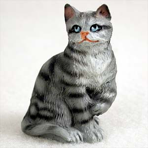 A detailed miniature cat figurine of a silver shorthaired tabby, designed as a decorative accent for bonsai or small displays. The small sculpture depicts the cat in a sitting pose with one front paw delicately curled up toward its chest. The figurine features a light grey base color with hand-painted dark grey or black tabby stripes throughout its body and tail. It has striking, large blue eyes outlined in black, a small orange nose, and tiny pointed ears. The cat's gaze is directed forward and slightly upward, and the textured surface of the figurine mimics the appearance of short fur. It is set against a plain, off-white background.
