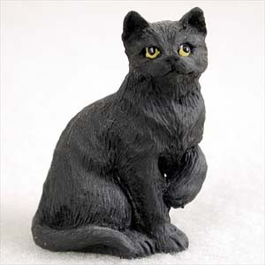 A detailed miniature figurine of a black cat sitting in an upright position on a plain, light-colored background. The figurine features realistic, textured black fur and has its front right paw slightly raised, as if caught in mid-motion while grooming. It has striking, round yellow eyes with dark pupils, giving it a lifelike expression. This decorative shorthaired tabby figurine is designed as a small-scale accessory, perfectly sized for adding character to a bonsai tree display or a miniature fairy garden.