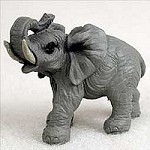 A detailed grey miniature elephant figurine, suitable for a bonsai tree display. The small elephant is captured in a dynamic pose with its trunk raised high and curled back towards its head, its mouth slightly open as if trumpeting. The figurine features realistic textures mimicking the wrinkled skin of an elephant, with large fan-like ears, sturdy legs, and small off-white tusks protruding from its face. Its dark eyes and intricately carved details add a lifelike quality. The figurine is set against a plain light-colored background, emphasizing its grey color and textured surface.