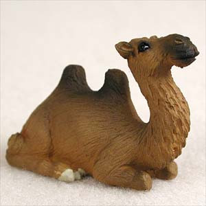 A detailed miniature figurine of a brown Bactrian camel, designed as a decorative bonsai tree accessory. The figurine features two distinct humps and is depicted in a resting, sitting position on a white textured surface. It is painted in warm brown tones with darker, realistic textured details representing thick fur on its neck, humps, and face, making it a perfect addition to a bonsai display or miniature garden scene.