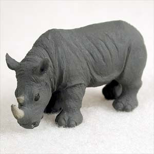 A miniature rhinoceros figurine crafted with realistic detail in a dark charcoal grey finish, featuring a textured surface that mimics the wrinkled skin of a real rhino. Designed as a decorative accessory for bonsai trees or miniature landscapes, the figurine is captured in a walking pose with its head lowered, highlighting its two distinct pale-colored horns and small ears as it sits against a plain, light-colored background.