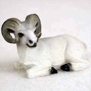A highly detailed miniature figurine of a Dall sheep ram, designed as a decorative accent for bonsai trees or miniature landscapes. The small white ram is shown in a peaceful resting position, lying down on its belly with its black-tipped hooves tucked neatly underneath. The figurine features intricately textured fur and large, majestic curved horns in shades of grey and tan. Its face is delicately painted with small dark eyes and subtle grey shading around the snout, giving it a realistic and serene appearance suitable for placement within a bonsai pot or terrarium.