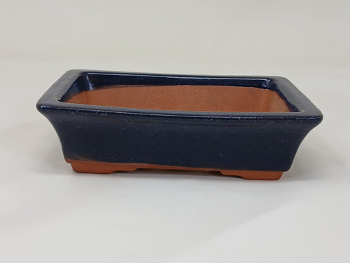 A 5-inch rectangular Yixing bonsai pot with a deep navy blue glazed finish. The pot is shown from a side angle against a neutral off-white background, highlighting its classic rectangular shape with flared sides and a wide, flat rim. The exterior is coated in a glossy, dark blue glaze that ends just above the base, revealing the natural, unglazed reddish-brown terracotta clay underneath. The interior of the pot is also unglazed, showing the matte texture of the Yixing ceramic. Four small, integrated feet at the corners elevate the pot slightly, which are also left in their natural earthy-brown clay color. This elegant ceramic container is designed for small bonsai trees, offering a striking contrast between the vibrant blue glaze and the warm, raw clay.