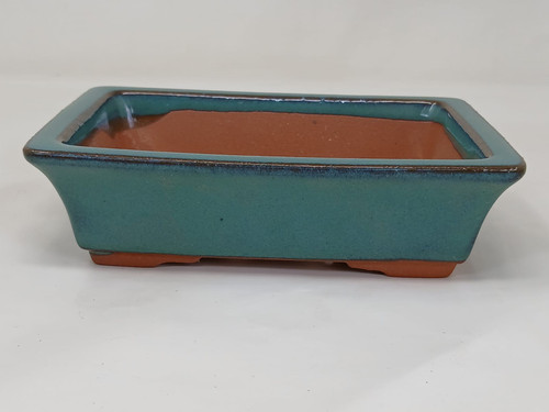 A detailed 5-inch Yixing bonsai pot featuring a rectangular shape with sides that flare gracefully outward toward the top. The exterior is coated in a vibrant, glossy teal-green glaze that stops just above the base, revealing the natural, unglazed reddish-brown clay characteristic of Yixing pottery. A thin, dark brown border highlights the upper rim, providing a sophisticated contrast to the green body. The interior of the pot also shows the earthy terracotta-colored clay at the bottom. The vessel sits on integrated feet, which are also left unglazed, and the entire pot is showcased against a clean, neutral white background, emphasizing its artisanal ceramic texture and classic design.