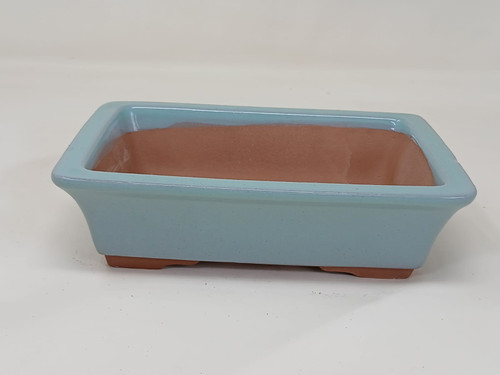 A detailed studio photograph of a 5-inch rectangular light blue glazed Yixing bonsai pot (model YX1130C) against a plain, off-white background. The pot features a soft, powder-blue glossy glaze with subtle speckling that covers the exterior sides and the flat, overhanging rim. The interior and the bottom edge of the pot are unglazed, revealing the natural, warm reddish-brown tone of the Yixing clay. The pot has a classic rectangular shape with slightly tapered sides and sits on four small, integrated feet designed to provide essential drainage and airflow for a bonsai tree's root system.