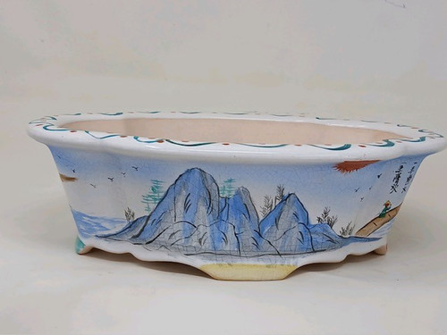 A detailed, eye-level studio shot of a 10-inch oval Yixing bonsai pot, showcasing a hand-painted traditional landscape scene. The ceramic pot features a white glaze with a delicate crazed texture, characterized by fine, web-like surface cracks that give it an antique appearance. The focal point is a vibrant landscape illustration in shades of blue, green, and black ink, depicting jagged mountain peaks, scattered pine trees, and a flock of birds in flight. On the right side, a small figure in a conical hat walks along a path under a setting red sun, accompanied by vertical black calligraphy. The pot is designed with a decorative scalloped or wavy rim and a matching undulating base supported by small, integrated feet. The interior of the pot is a natural, unglazed cream color, suitable for housing a bonsai tree. This artistic bonsai container combines the functionality of Yixing pottery with the aesthetic of classic Asian ink-wash painting.