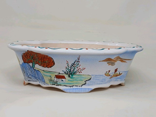 An eye-level, side-view photograph shows a 10-inch hand-painted Yixing bonsai pot featuring a shallow, oval body with a decoratively scalloped rim and matching lobed feet. The ceramic pot is finished with a glossy white glaze that displays a delicate crackle or crazing pattern across its surface.

The front of the pot is adorned with a colorful, traditional landscape scene. On the left, a large, vibrant orange-red tree stands behind a blue-tinted rocky formation. In the center, a quaint small house with a red roof sits on a green grassy bank next to another tree with green foliage and tiny red blossoms. To the right, two traditional sailing vessels glide across a calm blue sea beneath soft, earth-toned mountains in the background. A playful decorative border consisting of a wavy blue line and small red dots runs along the top edge of the rim, completing the elegant and artistic design of this bonsai vessel.
