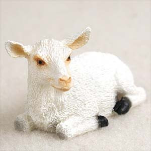 A detailed miniature figurine of a white goat, designed as an accessory for a bonsai tree or fairy garden. The goat is depicted in a resting pose, lying down with its head turned slightly to its left. It features textured white fur, black hooves, pointed ears, and light tan coloring around its nose and eyes. The figurine is shown on a plain, light-colored background, highlighting its realistic features and small scale.