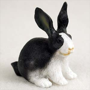 A detailed miniature figurine of a black and white rabbit, designed as a decorative accessory for a bonsai tree landscape. The figurine, resembling a Dutch rabbit, features a striking pattern where its tall ears, back, and sides are a deep black, while its face, chest, and front paws are a clean white. A prominent white blaze extends up its nose, and the small nose and mouth areas have subtle tan accents. The entire surface is finely molded with a realistic fur-like texture. The rabbit is captured in an alert, seated pose, looking slightly to the side. This charming animal statue is ideal for adding a sense of life and scale to miniature gardens, terrariums, or indoor bonsai displays.