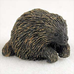 A detailed miniature figurine of a porcupine, specifically designed as a decorative bonsai tree accessory. The figurine is crafted with intricate textures to represent dense, dark brown and black quills with lighter tan highlights. It features a rounded face with small, shiny black eyes and a blunt nose, posed in a forward-crouching position with its paws tucked under its body. This small animal ornament, often referred to as a "mud man" style accessory, is used to add character and a sense of scale to a bonsai planter or miniature garden.