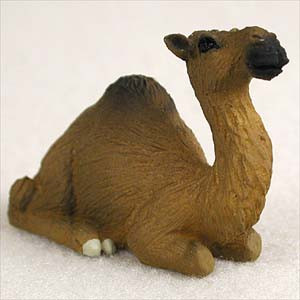A detailed figurine of a dromedary camel, designed as a decorative accessory for a bonsai tree or miniature landscape. The camel is depicted in a restful, kneeling position on a white, textured surface that resembles fine desert sand. Crafted with realistic details, the figurine features a single hump and is painted in shades of warm medium brown, with darker brown accents on the top of its hump and head to mimic the texture of thick fur. Its long, elegant neck curves upward, leading to a small face with dark eyes and a blackish-brown snout. Subtle white highlights at the base represent its tucked-under feet. This charming dromedary camel miniature is an ideal addition for creating a desert-themed scene within a bonsai display, terrarium, or fairy garden.