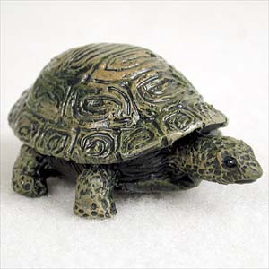 A detailed miniature turtle bonsai tree figurine with a highly textured, olive green and brown domed shell. The shell features intricate swirling patterns, and the turtle's head and thick legs are mottled with dark, realistic spots reminiscent of a tortoise. This small decorative accessory is shown from a three-quarter angle against a plain white background, highlighting the craftsmanship and lifelike appearance suitable for placement in a bonsai garden or terrarium.