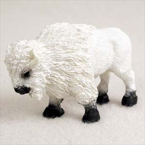 A detailed miniature figurine of a white buffalo, specifically designed as a decorative accessory for bonsai tree landscapes. The small bison is captured in a standing pose, facing slightly downward and to the left. Its entire body is covered in a highly textured, off-white finish that realistically mimics thick, shaggy winter fur, particularly around its large shoulder hump and head. Contrasting with its white coat, the figurine features solid black hooves and a dark black muzzle. This miniature animal adds a sense of scale and storytelling when placed at the base of a bonsai tree or within a miniature fairy garden scene.