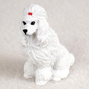 A detailed miniature figurine of a white poodle, sculpted in a sitting position and angled slightly to the left. The figurine is intricately textured to mimic thick, wavy, long white fur, particularly around the ears, chest, and legs, characteristic of a classic poodle grooming style. On the top of its head, nestled within the long fur of its topknot, is a tiny, vibrant red bow. The poodle features small, black, bead-like eyes and a tiny black nose, giving it a gentle expression. This small decorative accessory is designed to be placed within a bonsai tree arrangement or a miniature fairy garden to add a touch of personality and charm. The figurine is set against a soft, neutral, off-white background that emphasizes its clean white color and delicate details.