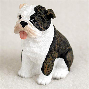 A detailed, miniature figurine of a sitting bulldog puppy, designed as a decorative accessory for a bonsai tree display. The small dog features a classic bulldog appearance with characteristic facial wrinkles and skin folds. It is colored with a mix of bright white and dark brindle patterns; white covers its chest, front legs, and the left side of its face, while a deep brindle—a mix of black and brownish-red stripes—marks its right eye area, ear, and back. The puppy has a cheerful expression, with its pink tongue playfully sticking out of the side of its mouth. The figurine has a textured surface to mimic short fur and is set against a neutral, light-colored background, highlighting its suitability as a charming hand-painted ornament for indoor gardens or desktop decor.
