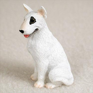 A detailed miniature Bull Terrier figurine designed as a bonsai tree accessory. This white dog figurine is shown in a sitting position, facing toward the left. It features the breed's iconic egg-shaped head, pointed ears, and a prominent black patch surrounding its left eye. The figurine has a finely textured surface mimicking a short coat, a small black nose, and a pink tongue slightly peeking out of its mouth. The background is a soft, neutral beige, highlighting the fine details of this small collectible animal miniature.