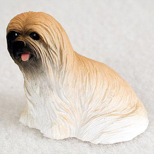 A detailed miniature figurine of a Lhasa Apso dog, designed as a charming decorative accessory for a bonsai tree or miniature indoor garden. The figurine captures the breed's signature look with a long, floor-length coat featuring finely molded vertical textures that mimic flowing, silky hair. The coloring transitions from a warm honey-tan on the crown of the head and upper back to a bright white towards the base. The dog’s face features a dark, black-masked muzzle and eye area, contrasted by a tiny, playful pink tongue peeking out of its mouth. The figurine is shown from a side profile in a resting position against a neutral, textured white background, highlighting its compact, rounded shape and the intricate details of the painted resin.