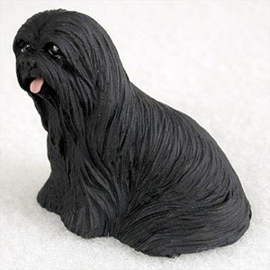 A detailed miniature figurine of a black Lhasa Apso dog, specifically designed as a decorative accessory for a bonsai tree display. The figurine is shown in a seated pose, facing slightly to the left, and features an intricately textured, long, flowing coat that mimics real dog hair. Its solid black color is matte, with small, dark eyes and a tiny pink tongue sticking out from its mouth, adding a playful touch. This small dog statue is photographed against a neutral, off-white textured background, highlighting its craftsmanship and suitability as a miniature garden ornament.