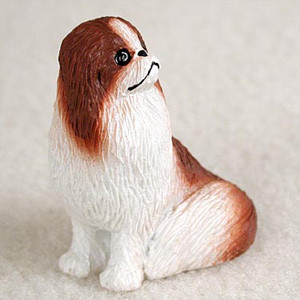 Miniature red and white Japanese Chin figurine seated, looking up and to the side