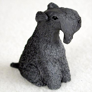 A detailed miniature figurine of a Kerry Blue Terrier dog, designed as a decorative accessory for a bonsai tree. The figurine is depicted in a sitting pose, with its head turned slightly to the right. It is crafted in a solid, dark charcoal gray color and features the breed's characteristic curly, textured coat, which is rendered with fine, wavy details across its entire body. 

The figurine captures the distinctive long muzzle with a thick "beard" and prominent eyebrows, along with small ears that fold forward over the head. A single small, black, glossy eye is visible, adding a lifelike quality to the piece. Set against a plain, off-white, slightly textured background, this miniature Kerry Blue Terrier statuette is a charming addition to an indoor bonsai display or a miniature garden scene, providing a touch of personality and scale.