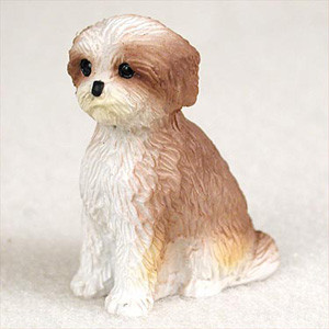 A detailed miniature Shih Tzu figurine designed as a decorative accessory for a bonsai tree arrangement. The small dog is sculpted in an upright sitting position, featuring a "sport cut" groomed coat. Its coloring is a mix of warm tan and white, with the tan concentrated on its floppy ears and along its back, while its face, chest, and front legs are primarily white. The figurine has realistic details, including a textured fur pattern, tiny glossy black eyes, and a small black nose, adding a whimsical sense of life and scale to a miniature landscape or indoor bonsai display. Combined with the neutral off-white background, the focus remains on the craftsmanship of the dog figurine.