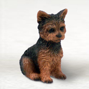 A detailed miniature figurine of a Yorkshire Terrier puppy, specifically designed as a decorative bonsai tree accessory. The hand-painted ornament features a realistic "puppy cut" style, with intricate, textured fur details. The puppy is shown in a sitting pose, facing slightly to the right, with a combination of black fur across its back and head and warm tan or ginger colors on its face, chest, and legs. Its dark, expressive eyes, small black nose, and alert, pointed ears give it a lifelike appearance. This small collectible is set against a clean, neutral white background, highlighting its craftsmanship as a charming addition to any miniature garden or bonsai landscape.