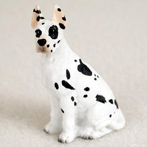 A detailed miniature figurine of a Harlequin Great Dane, designed as a decorative accessory for a bonsai tree. The small dog statue features a white coat with distinct black spots, typical of the harlequin pattern, including a prominent patch over its left eye and smaller spots scattered across its body and tall, pointed ears. It is depicted in a regal, upright sitting position on a neutral background, ready to add a touch of personality to a miniature garden or bonsai display.