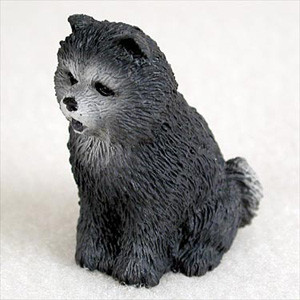 A detailed miniature figurine of a blue Chow Chow dog, designed as an accent piece for a bonsai tree arrangement. The figurine depicts the dog sitting in an upright, attentive pose with its mouth slightly open as if mid-bark. The coloring is a deep charcoal grey with lighter, smoky-silver highlights around the muzzle and chest, mimicking the "blue" coat color characteristic of the breed. The surface is intricately molded to show the texture of dense, fluffy fur. This small bonsai accessory features the breed's distinctive small triangular ears and a thick, bushy tail curled against its side, providing a charming and realistic touch to a miniature garden or bonsai display.