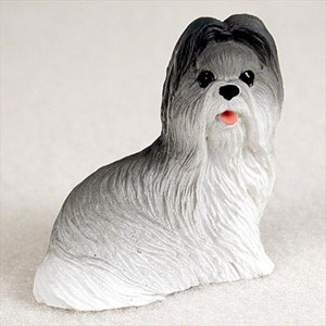 A small, detailed figurine of a Shih Tzu dog, designed as a decorative accessory for bonsai trees or miniature gardens. The figurine features the breed's signature long, flowing coat, which is textured to look like real fur. The coloring has a soft gradient effect, with dark charcoal gray on the top of the head and ears that gradually transitions into light gray and then a crisp white along the chest and body. The dog's face is characterized by two small, glossy black eyes, a tiny black nose, and a slightly open mouth where a small, bright pink tongue is visible. The figurine is depicted in a seated position, looking forward against a neutral, off-white background, emphasizing its use as a charming accent piece for indoor plants.