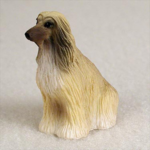 A detailed, miniature figurine of an Afghan Hound dog, specifically designed as a decorative accessory for a bonsai tree arrangement. The figurine is shown in a sitting profile pose, highlighting the breed’s characteristic long, flowing coat textured with realistic tan and off-white fur details. It features a slender muzzle with a black nose and long, dark-tipped ears. The miniature sits on a neutral, textured white surface, emphasizing its small scale and suitability for placement within a bonsai pot or miniature garden landscape.