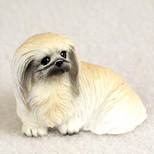 A detailed miniature figurine of a Pekingese dog, specifically designed as a decorative accessory for a bonsai tree arrangement. The figurine shows the dog lying in a calm, alert pose with its front paws visible underneath its chest. The long, flowing coat is meticulously textured and painted in realistic shades of cream and light buff, transitioning to darker grey and black fur around the muzzle and large, expressive dark eyes. This small Pekingese statue is set against a neutral, light-textured background, highlighting its intricate hand-painted details and making it a perfect addition to a miniature garden or indoor bonsai display.