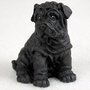 A detailed matte black figurine of a Shar-Pei puppy, depicted in a sitting position. The miniature sculpture intricately captures the breed's characteristic deep skin folds and heavy wrinkles across its entire body, especially concentrated around the head, neck, and shoulders. It features a broad muzzle, small triangular ears that fold forward, and large, dark, glossy eyes that catch the light. The uniform black color of the figurine is set against a neutral, light-colored background, highlighting its texture and form as a decorative accessory for a bonsai tree arrangement.