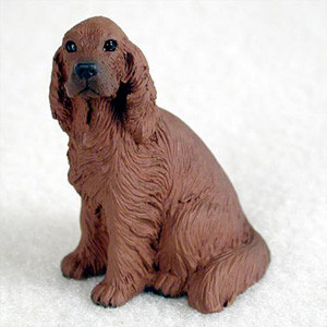 A detailed miniature figurine of an Irish Setter, specifically designed as an accessory for bonsai tree displays. The figurine captures the breed's iconic features with a rich, mahogany-colored coat molded to show the texture of its long, wavy, and feathery fur. The dog is depicted in a seated, attentive pose with its long ears framing its face, soulful dark eyes, and a prominent black nose. Its tail is neatly tucked around its side. The small-scale statue is set against a plain, light-colored background, highlighting the craftsmanship and lifelike detail that make it a charming addition to a miniature bonsai garden or a thoughtful gift for pet lovers.