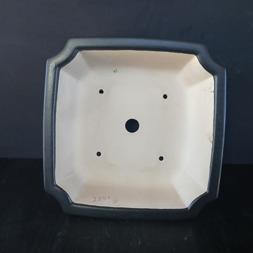 Top-down view of a 9-inch square Yixing ceramic bonsai pot, model No. 2281D. The pot features a wide, charcoal-gray matte-glazed rim with elegant notched corners, giving it a classic lobed appearance. Looking into the pot, the interior is unglazed, revealing the natural light cream-colored Yixing clay. The base of the interior shows a large central drainage hole and four smaller, circular wire holes positioned toward each corner to help secure a tree's root ball. Near the bottom edge, the identification number "2281 D" is handwritten in red. The pot is centered in the frame against a dark background, emphasizing its geometric structure and functional design for bonsai cultivation.
