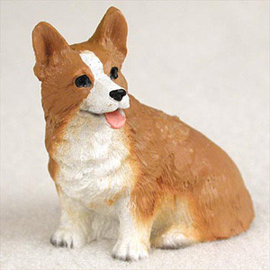 A detailed miniature figurine of a Pembroke Welsh Corgi, designed as a decorative accessory for a bonsai tree or fairy garden. The hand-painted figurine depicts a sitting Corgi with a happy expression and its pink tongue slightly peeking out. It features the breed's characteristic large, upright ears and a coat with textured fur details in traditional tan and white colors. White markings are visible on its chest, front paws, and as a blaze across its snout and forehead, contrasting with its warm ginger-colored body. The figurine is shown against a plain, light-colored background, emphasizing its small scale and intricate craftsmanship.