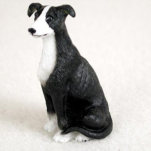 A detailed miniature black and white Greyhound dog figurine sitting in an upright, alert position. The small figurine features a textured coat that mimics the appearance of fur, with a striking tuxedo pattern: a solid black body, head, and ears contrasted by a white blaze on the face, a white chest, and white paws. This decorative bonsai tree accessory is designed to add a realistic touch to indoor gardens, miniature landscapes, or terrariums, and is shown set against a neutral, soft-white background.